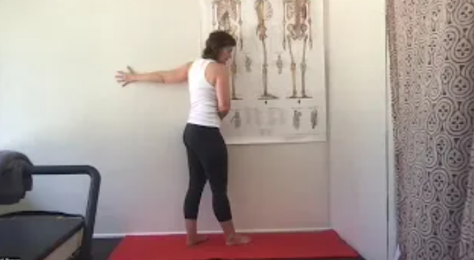 A woman doing a pec stretch against a wall.